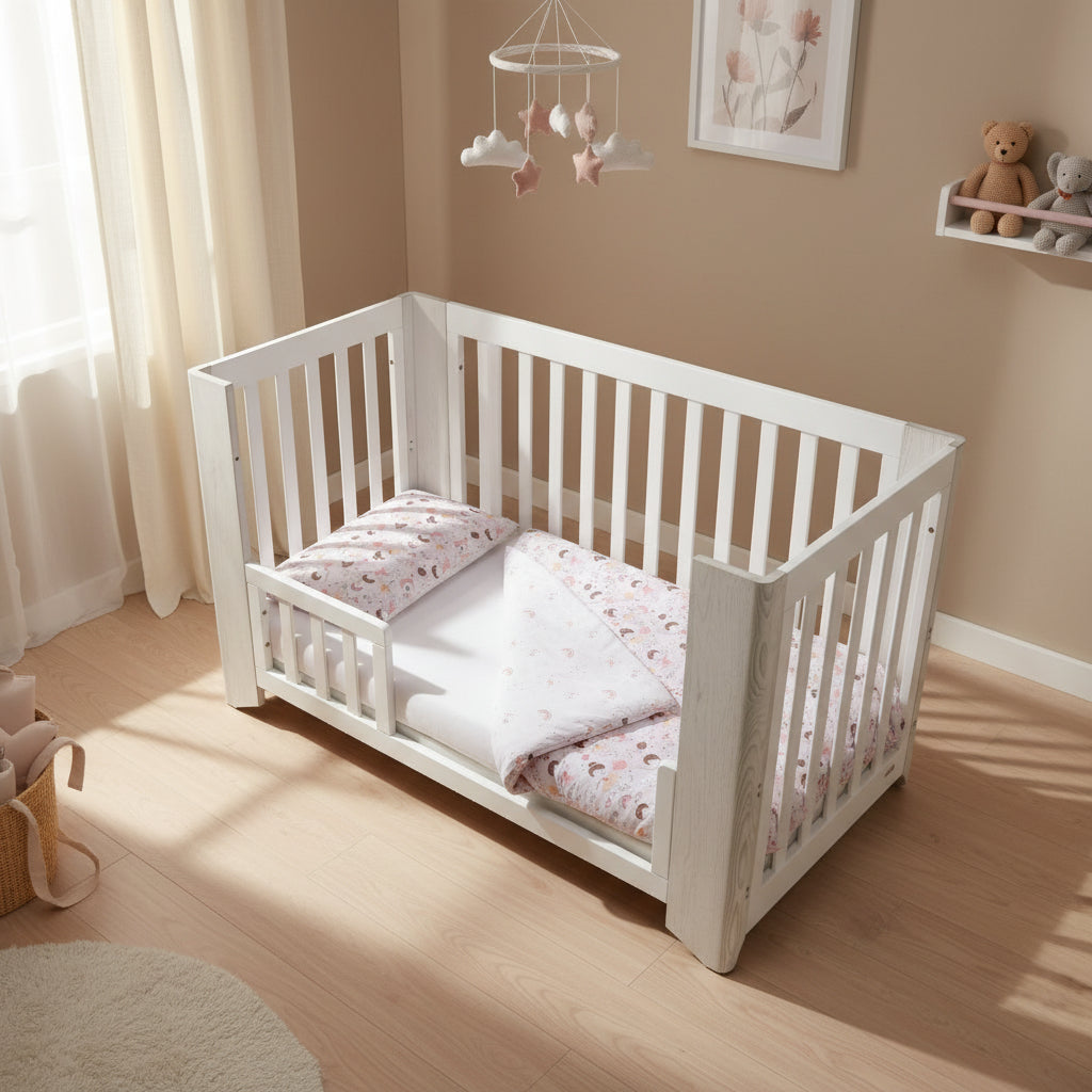 White crib with pink and white baby bedding set on a white background