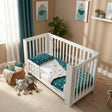 White crib with teal bedding in a child's room with toys and decor.