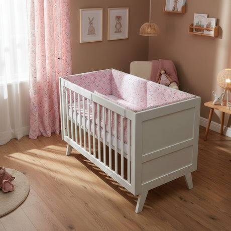 Crib with pink floral and animal patterned bedding set on a white background
